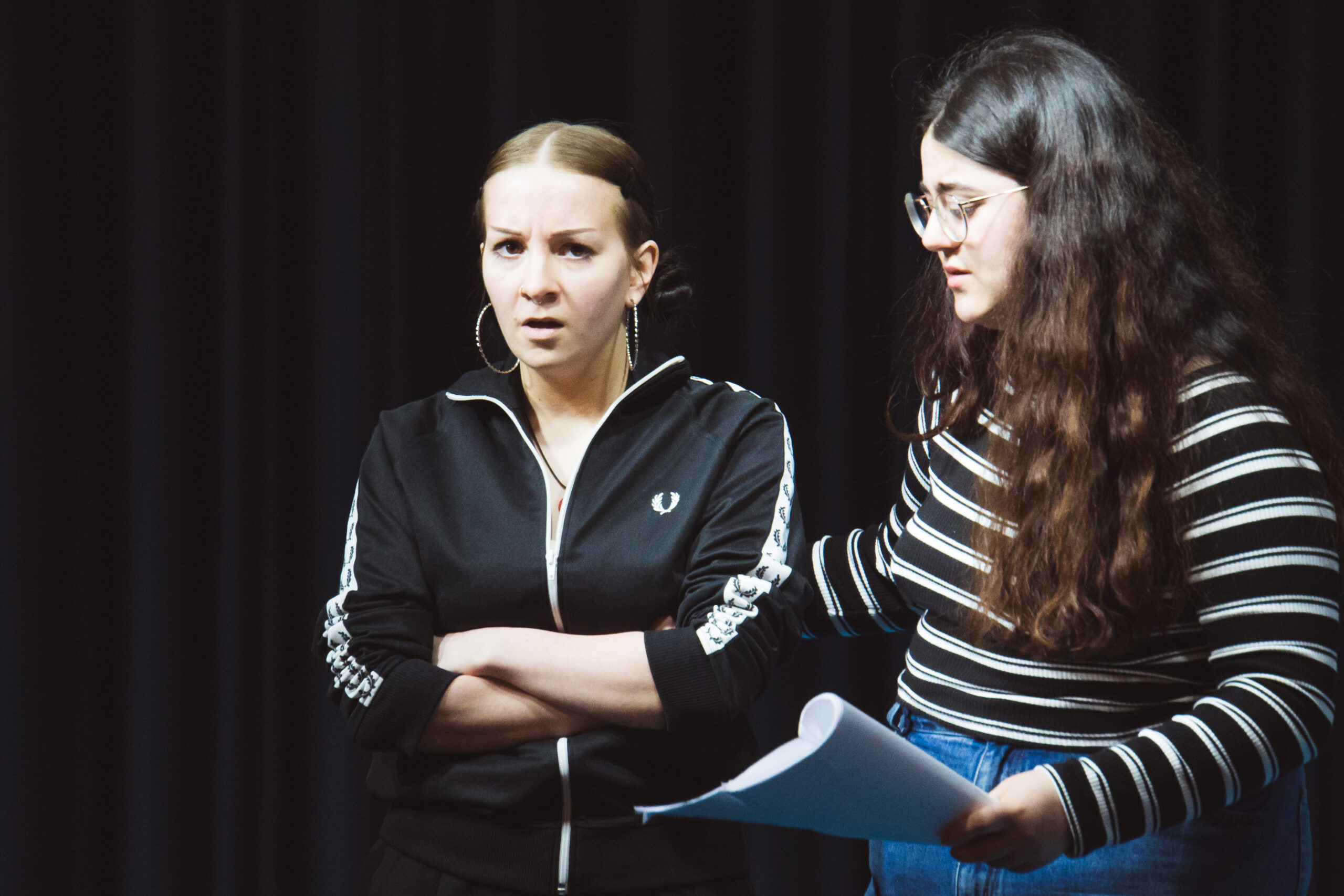 Das brennende Dorf - Probeneindrücke - zwei Schauspielerinnen auf der Bühne; Schauspielerin links im Bild verschränkt ihre Arme