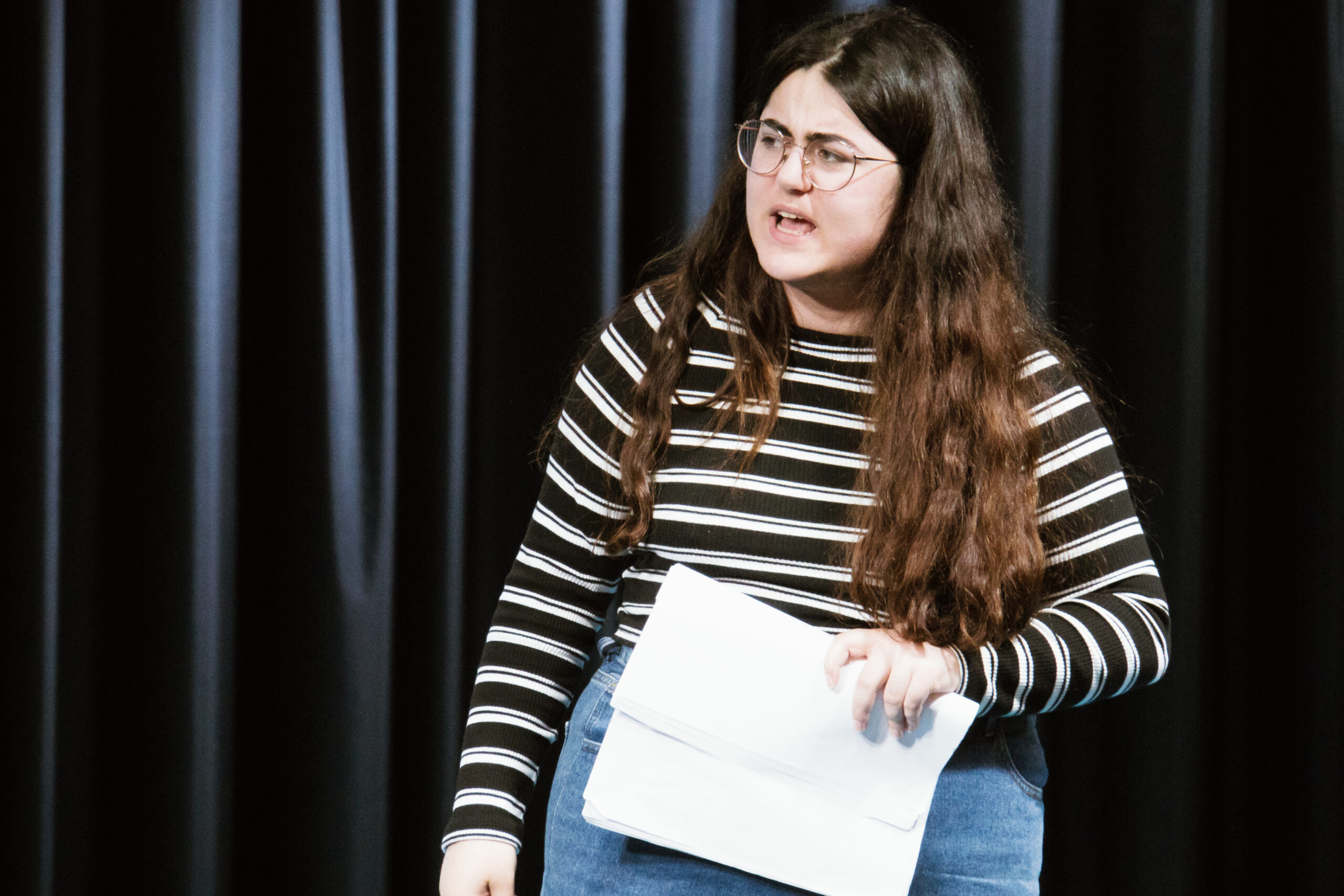 Das brennende Dorf - Probeneindrücke - Schauspielerin mit Textbuch auf der Bühne; sie hat einen verärgerten Gesichtsausdruck